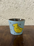 Handmade ceramic mug with cute yellow banana design, stars, light blue speckled glaze, perfect for coffee or tea