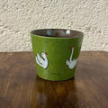 Green ceramic mug with white swan designs, handmade and food-safe, perfect for tea or coffee.