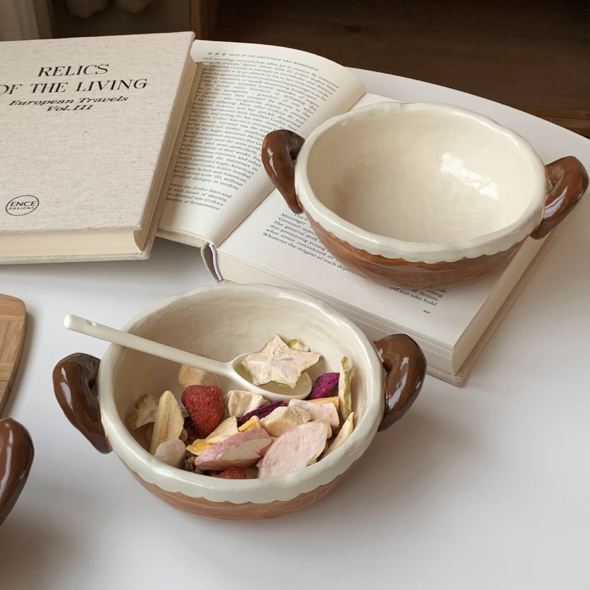 Handmade ceramic bowls with dried fruit, styled beside an open book for cozy tea moments.
